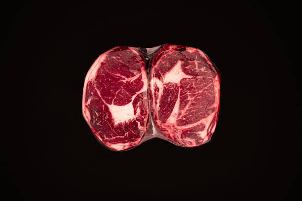 Assortment of raw beef steaks and pork ribs in vacuum sealed plastic packaging.