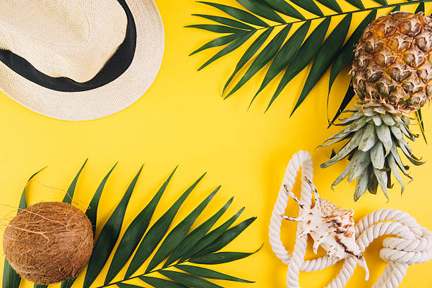 Tropical fruits, beach accessories, and palm leaves on a vibrant yellow background, symbolizing summer vacation