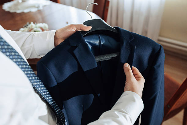 A man is holding a blue jacket on a hanger. The jacket is hanging on a wooden chair