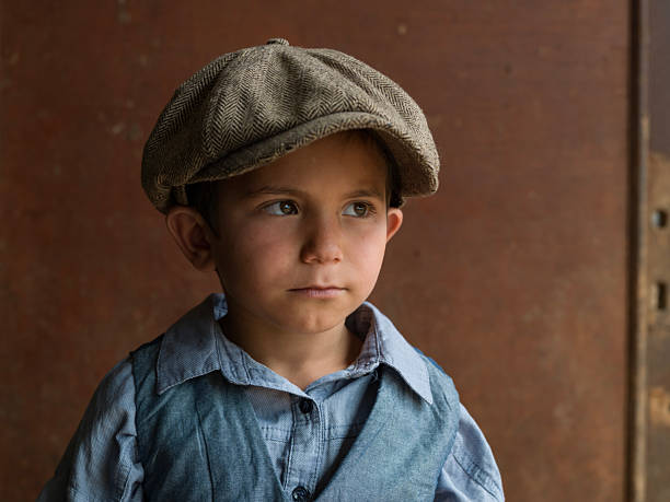 Portrait of cute 6 years old boy wearing a brown newsboy cap, gray shirt and waist. Shot under natural light with a medium format camera.