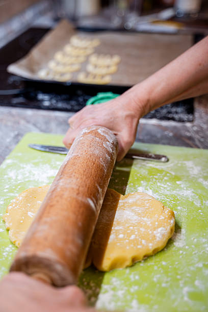Flour, eggs, and butter are arranged on a table as dough is rolled out for Christmas cookies. Festive cookie cutters and other baking tools suggest a cheerful holiday atmosphere in the kitchen.