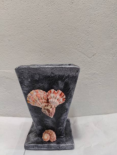 This gracefully textured grey vase is beautifully adorned with a cluster of seashells on its front, offering a sophisticated and natural touch to home decor.