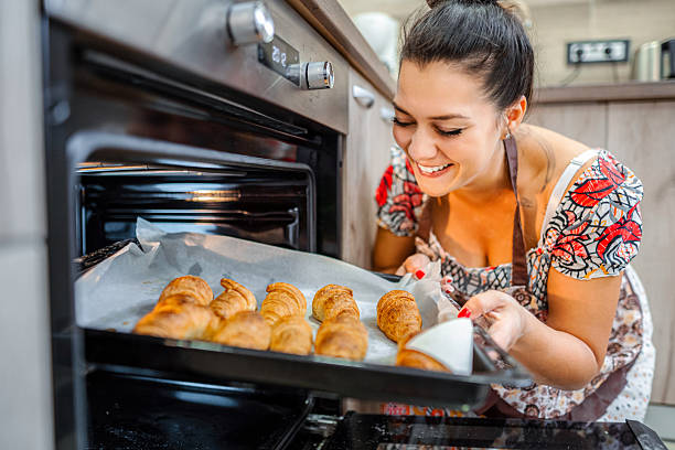 Woman smiling while baking fresh croissants in kitchen oven