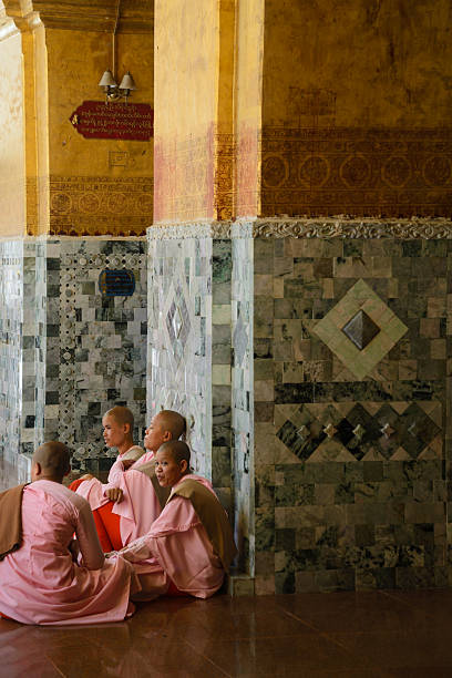 Close up of a group of 4 nuns (thisahin) with the traditional pink and orange uniform and shaved head, sitting on the floor of the temple coumpound