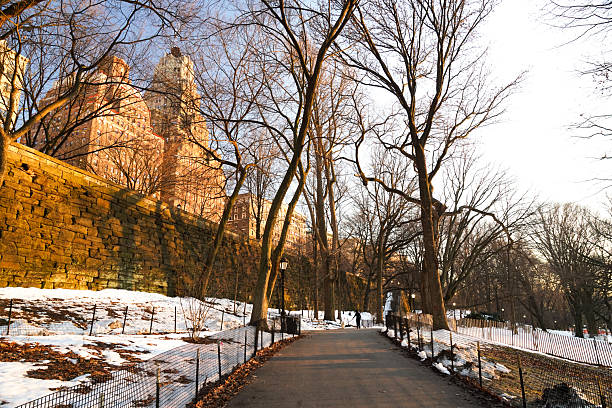 Golden hour light highlighting the tall, brick buildings and the tops of trees sitting up above the walking path that’s surrounded by snow