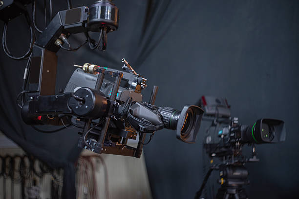 Two professional digital broadcast cameras in a dark television studio, one on a gimbal stabilizer, behind the scenes shot