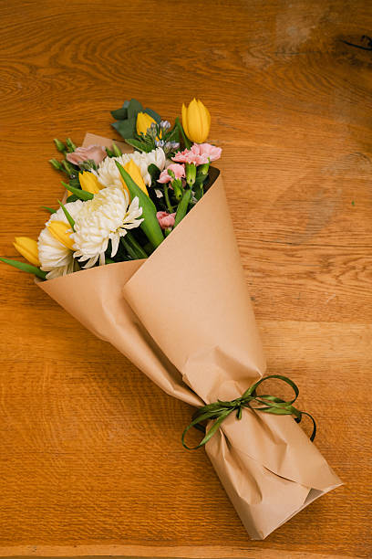 Fresh flower bouquet wrapped in craft paper on wooden table