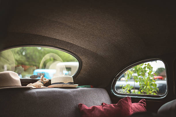 The interior of the vintage car features hats and a small dog figurine on the back seat, with a view of the outside world