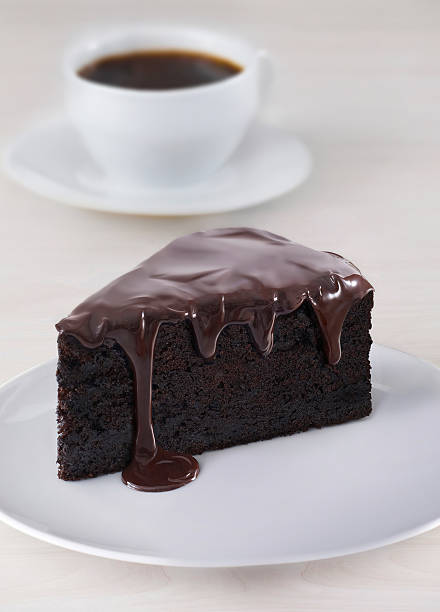 Slice Of Chocolate Cake With Dripping Ganache And Coffee Cup In Background