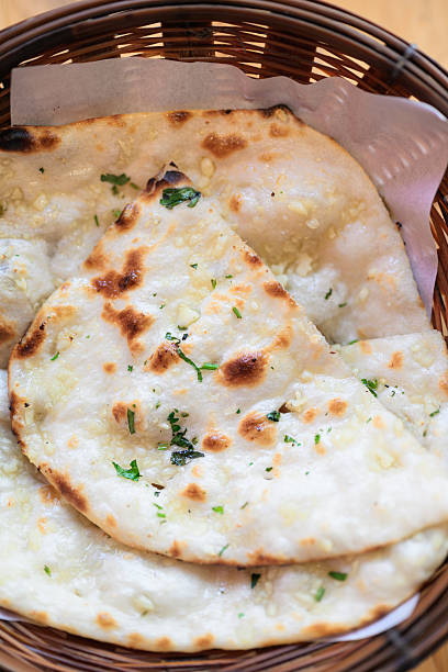 Close-up of freshly baked garlic naan bread served in a wicker basket on a wooden table