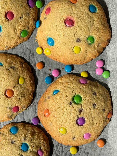 Image of vibrant cooked rainbow chocolate chip cookies / colourful biscuits made from cookie dough, loaded with candy and sweets