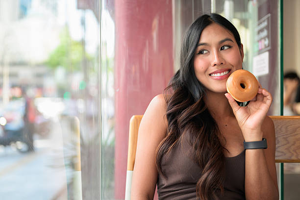 Smiling Woman Holding Glazed Donut in Cafe