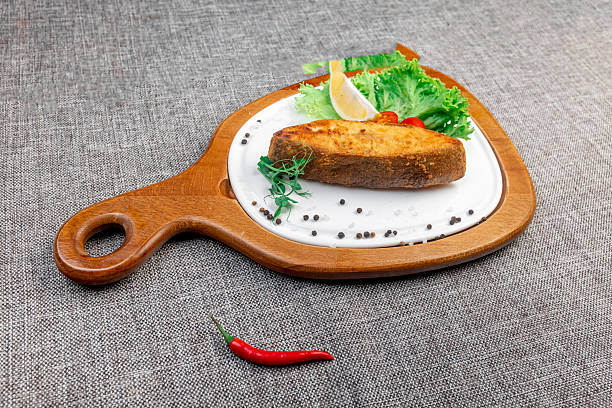 Appetizing fried halibut steak with lemon and vegetables on a wooden board.