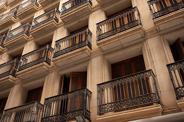 Residential building facade showcasing rows of elegant wrought iron balconies and traditional wooden shutters, some partially open, creating a detailed pattern of architecture