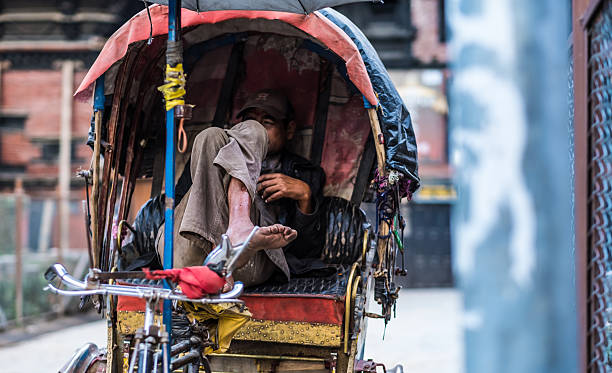 Kathmandu, Nepal - 06 October 2017: Middle-aged rickshaw driver sits with crossed legs in the cabin of his rickshaw and waits for clients.