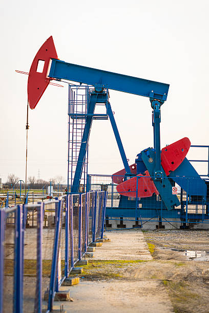 Silhouette of an operating oil pumpjack extracting crude oil from the ground during sunset. Warm golden light creates a dramatic industrial landscape, symbolizing petroleum production, energy resources, fossil fuels, and the global oil industry. Suitable for themes of energy economy, natural resources, and industrial infrastructure.