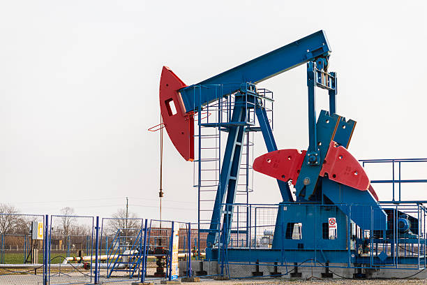 Silhouette of an operating oil pumpjack extracting crude oil from the ground during sunset. Warm golden light creates a dramatic industrial landscape, symbolizing petroleum production, energy resources, fossil fuels, and the global oil industry. Suitable for themes of energy economy, natural resources, and industrial infrastructure.