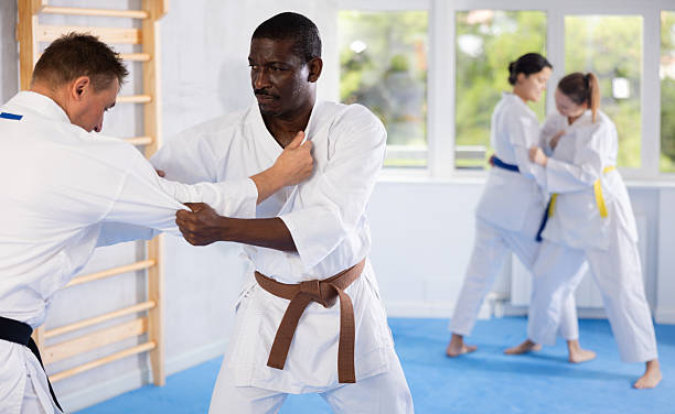 Judo or jiu-jitsu classes - two men practicing grabbing and throwing on sports mats under the guidance of a trainer