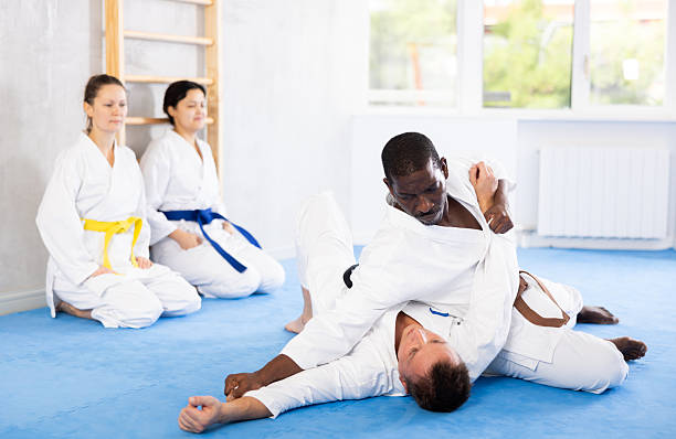 Judo or jiu-jitsu classes - two men practicing grabbing and throwing on sports mats under the guidance of a trainer