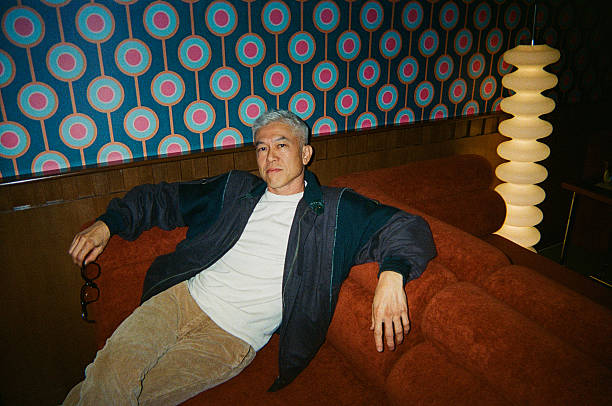 Mature Asian man relaxing on a sofa in a retro lounge interior while holding sunglasses, creating a stylish boutique lifestyle and travel atmosphere with instant film aesthetic, Kuala Lumpur