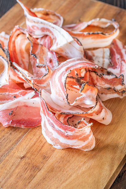 Rustic presentation of sliced Italian pancetta arranged neatly on wooden cutting board