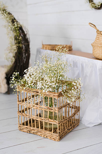 Rustic wicker basket holding a glass vase with delicate white flowers, perfect for country style interiors, wedding decor, or cozy home arrangements.