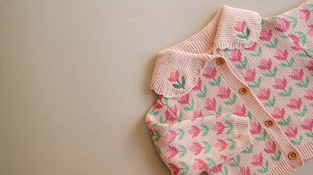 A close-up view of a soft pink knit cardigan featuring a repeating tulip floral motif and a scalloped collar with embroidered accents