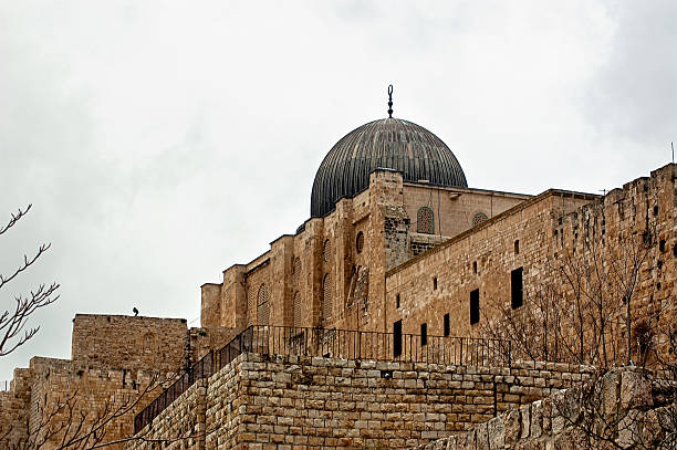 Iconic view of Al-Aqsa Mosque in Jerusalem, Israel with gray dome, stone walls, and railing under cloudy sky. Captures historical Islamic religious architecture for cultural heritage, travel tourism, education, and editorial applications.