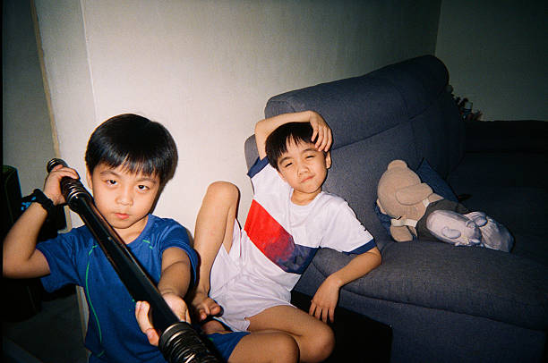 Two Asian boys sitting on a sofa and playing together indoors at home, representing childhood friendship, imagination, and playful moments between children, Kuala Lumpur