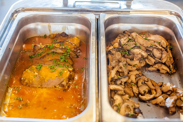 Sliced meat in gravy and sauteed mushrooms in stainless steel buffet