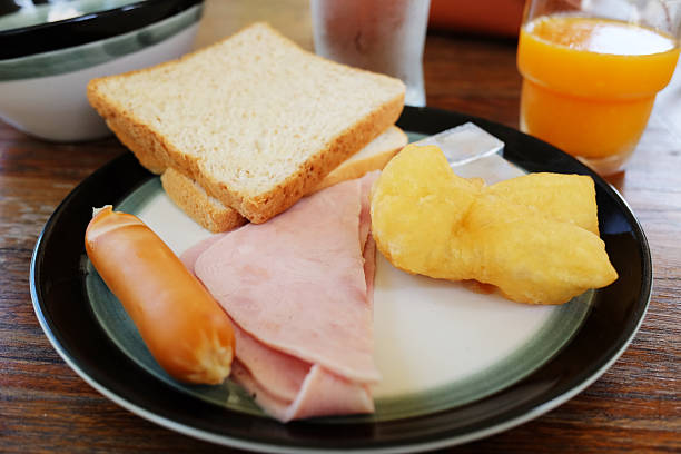 Scrambled eggs and toast with crispy bacon and hot dog in white dish served on a rustic wooden table for homemade breakfast