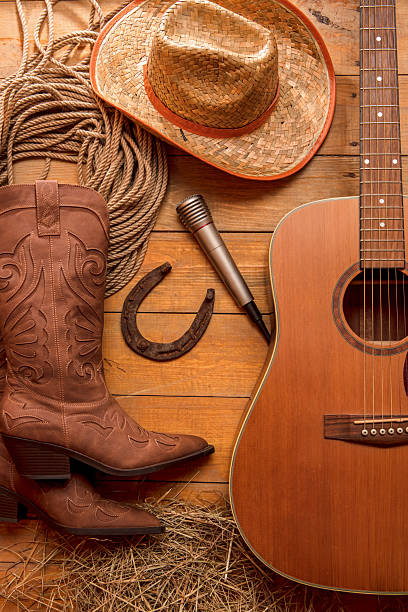 Acoustic guitar, rope, old rusty horseshoe, microphone, cowboy hat and boots on a barn wood texture background. American Country music concept.