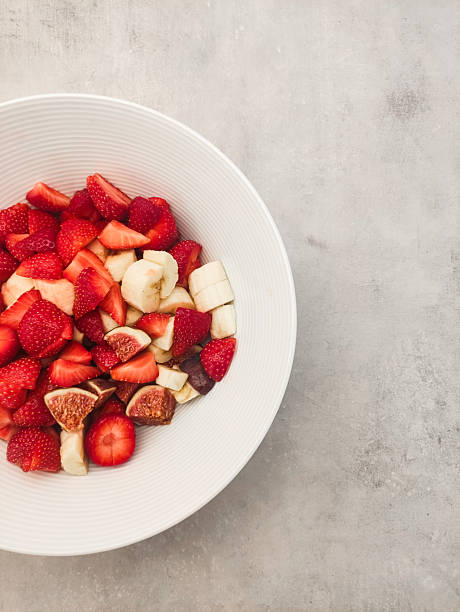Freshly sliced strawberries, bananas, and figs in a white bowl on textured gray surface showcasing healthy snack concept