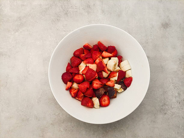 Freshly cut strawberries and bananas in a white bowl on textured gray surface showcasing healthy snack option