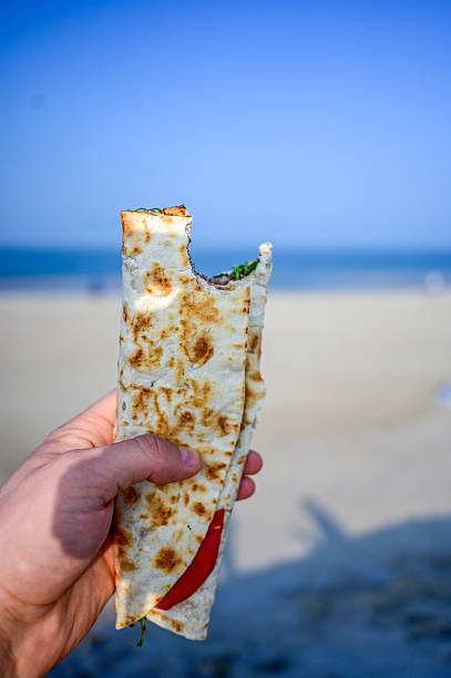 Hand holding piadina Italian flatbread sandwich at beach