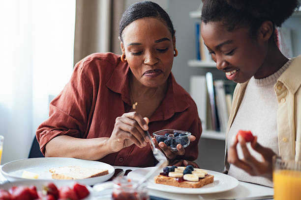 Mother and Teenage Daughter Sharing Breakfast Together at Home, Smiling and Preparing Fruit Toast