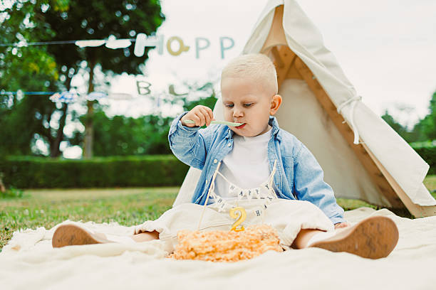 An adorable little toddler joyfully celebrating their 2nd birthday, surrounded by delightful cake in a cozy woodland setting that creates a perfect atmosphere for family and friends to enjoy together
