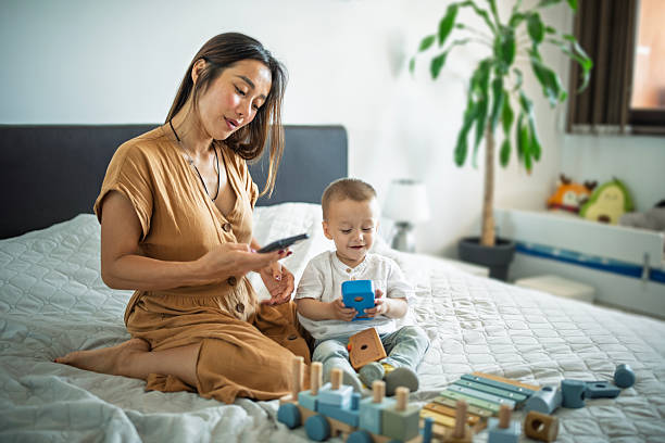 Asian mom using her phone while taking care of her baby by at home.