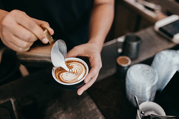 Barista skillfully pours steamed milk into espresso creating intricate latte art pattern