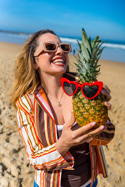 Woman holding pineapple wearing heart sunglasses on beach