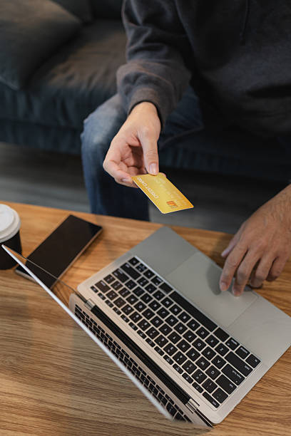 Man holding credit card while using laptop for online payment and digital shopping, representing ecommerce transaction, internet banking and modern financial technology.