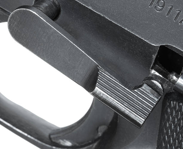 The slide stop on a pistol that is styled after the 1911 and semi-automatic seen in a close-up as it is being pulled out of the firearm for field stripping.