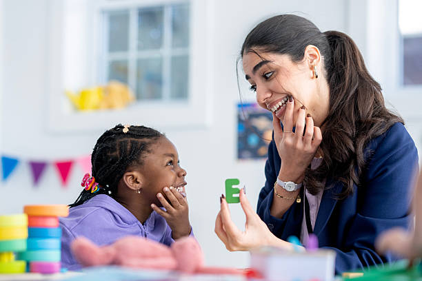 Hispanic female teacher and smiling Black girl student share a joyful moment while practicing the letter E in a colorful preschool classroom, illustrating early literacy, inclusive education and child-centered learning.