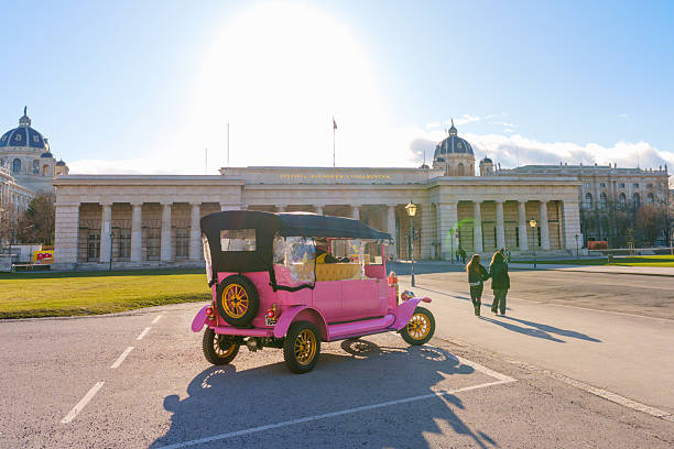 Vienna, Austria - February 24, 2026: Pink vintage sightseeing car parked at Heldenplatz square in Vienna, featuring the historic Outer Castle Gate and museum in the background.