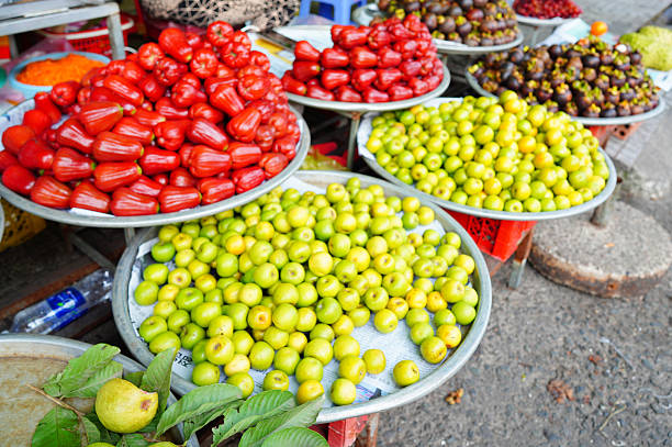 Tropical fruits typical of Southeast Asian markets. Large, bright red, cone-shaped fruits reminiscent of bell peppers. Chompoo (Pink Apple or Wax Apple) and Jujube (Chinese Date): Greenish-yellow, round fruits sales at Asian market in Vietnam.