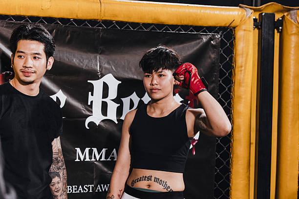 Martial arts athletes prepare for competition at an MMA event in a training facility with a cage and banners in view