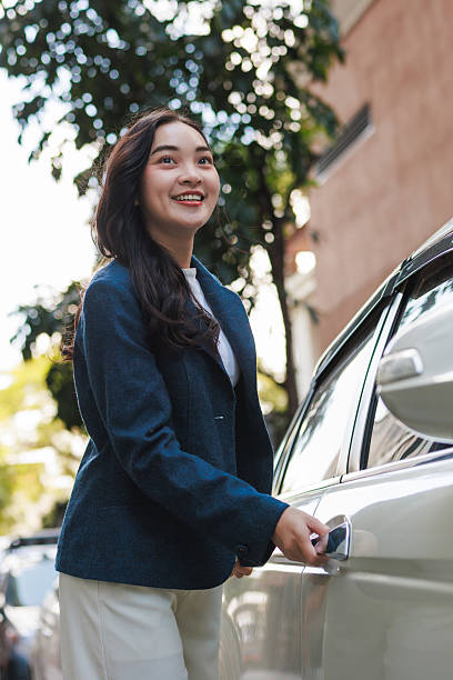 Young asian businesswoman smiling opening car door