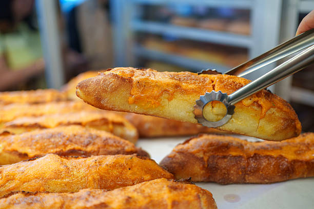 Customer using tongs to pick up a fresh mentaiko baguette in a bakery