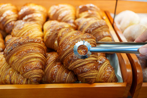 Freshly baked croissants being picked with tongs in a bakery
