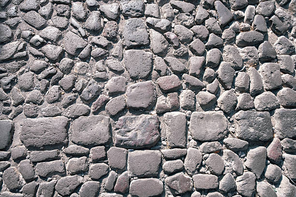 A top-down detailed shot of a vintage cobblestone pavement in the historic colonial city of Antigua, Guatemala. The image features uneven, dark volcanic stones arranged in a rustic pattern, reflecting the centuries-old urban infrastructure of this UNESCO World Heritage site. Ideal for backgrounds, travel editorial, or architectural textures.